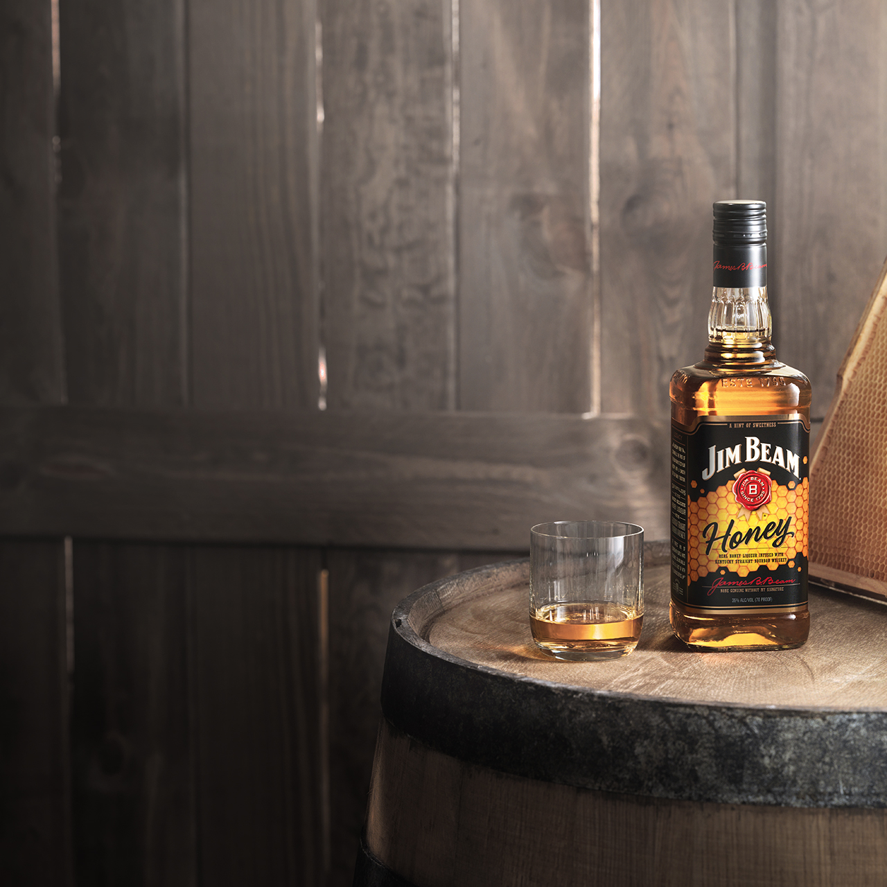 Uma garrafa de Jim Beam® Honey rodeada por barris de bourbon do Kentucky armazenados.
