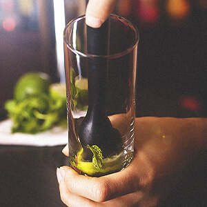 A bartender is muddling ingredients for a Jim Beam® drink at the bottom of a mixing glass.